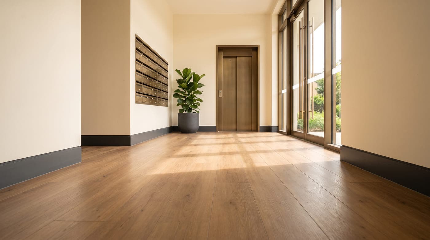 Ground-floor lobby of an Australian apartment building with large-format timber-look vinyl plank flooring, bronze mailboxes and a lift