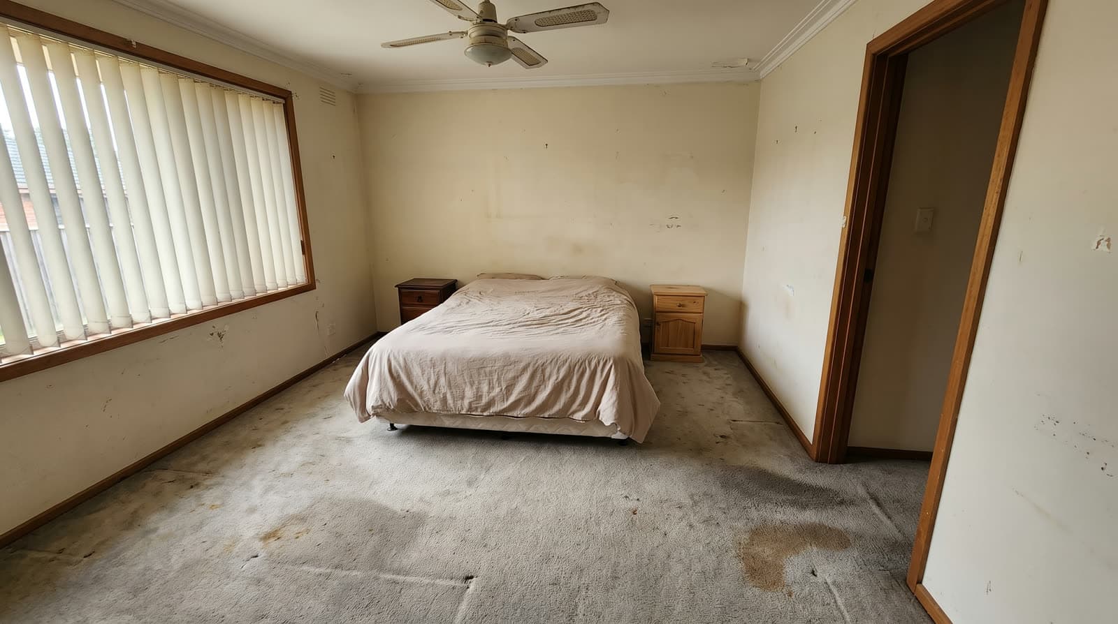 Bedroom before renovation — flattened stained carpet and dated vertical blinds