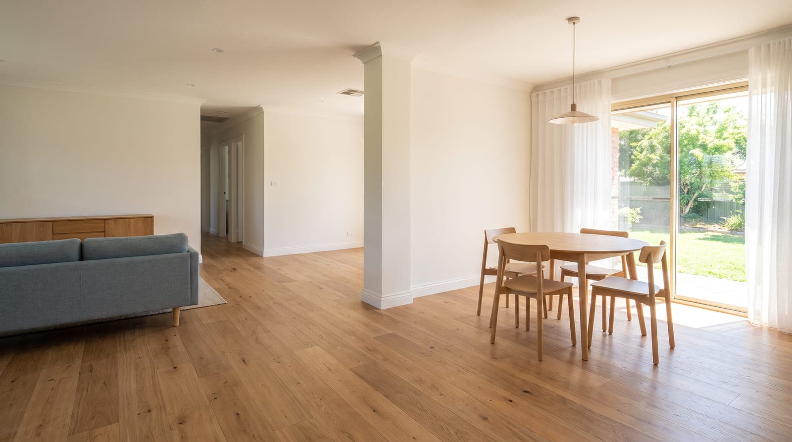 The same living and dining area after renovation, with wide-plank European oak engineered flooring and fresh white paint