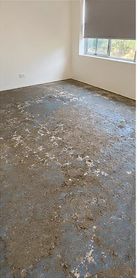 A concrete slab patched with old blue adhesive, scratched and uneven across the room.