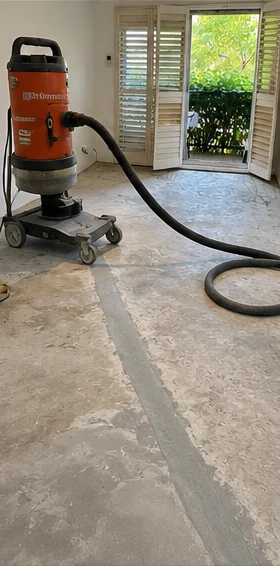 A dust-extracted floor grinder on the slab, with a repaired crack line running the length of the room.